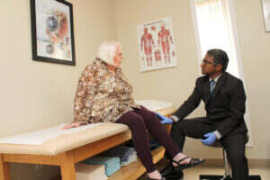 Michigan orthopedic surgeon sits on stool in front of exam table examining patient's knee. Orthopedics care includes hip replacement, sports medicine and more.